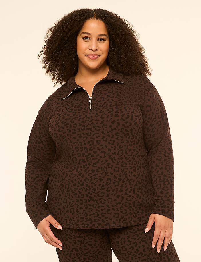 A woman with curly dark hair smiles at the camera, wearing a brown leopard-print quarter-zip sweatshirt and matching pants against a plain cream background.