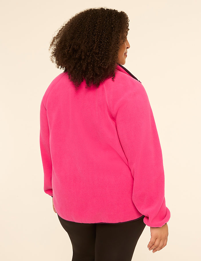 A woman in a bright pink fleece jacket and black leggings stands against a plain, light-colored background.