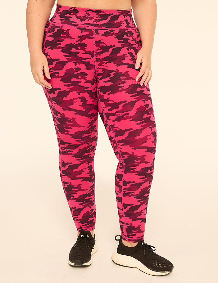 A person wearing pink camouflage leggings and black sneakers stands against a plain, light-colored background.