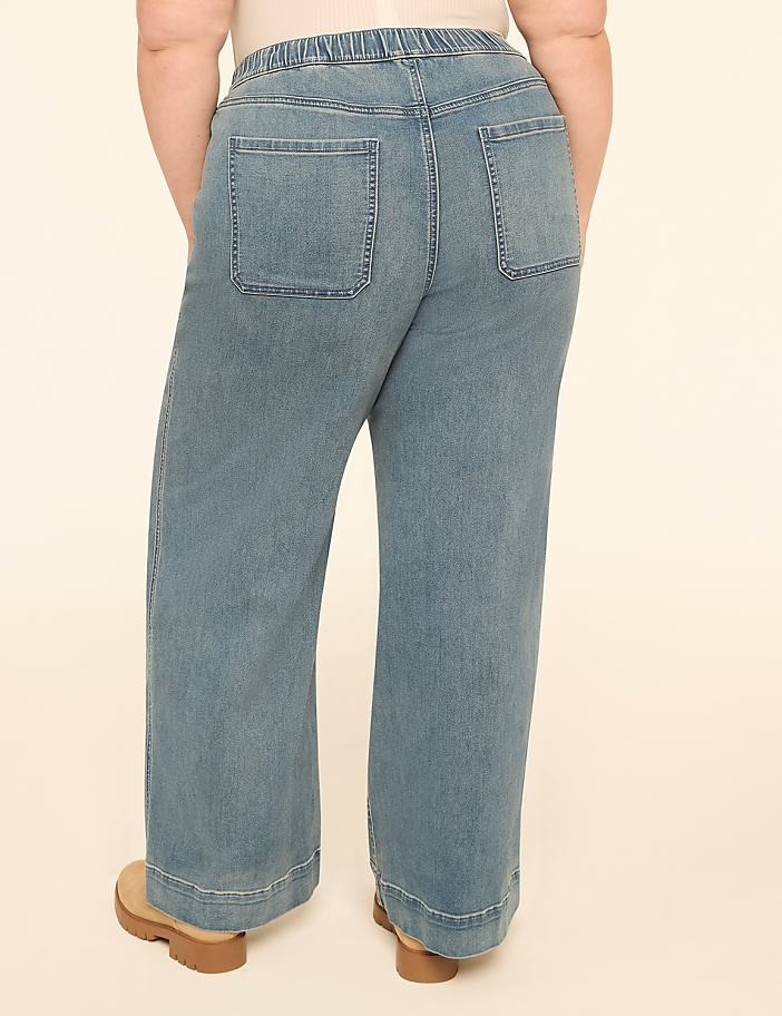 A person wearing light blue wide-leg jeans stands against a plain, light-colored background.