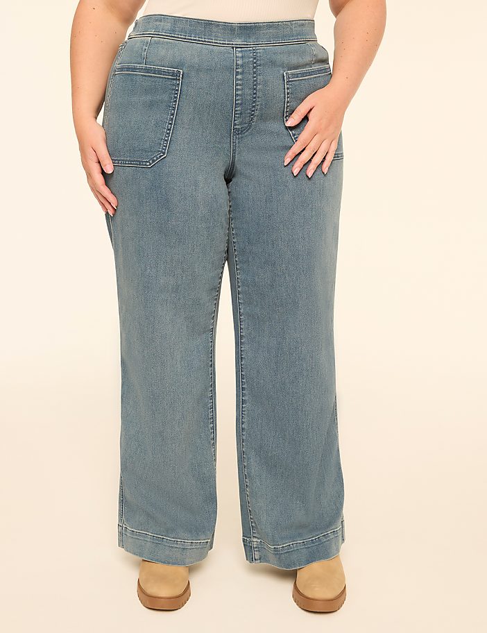 A person stands in light blue wide-leg jeans with tan shoes against a plain cream background.