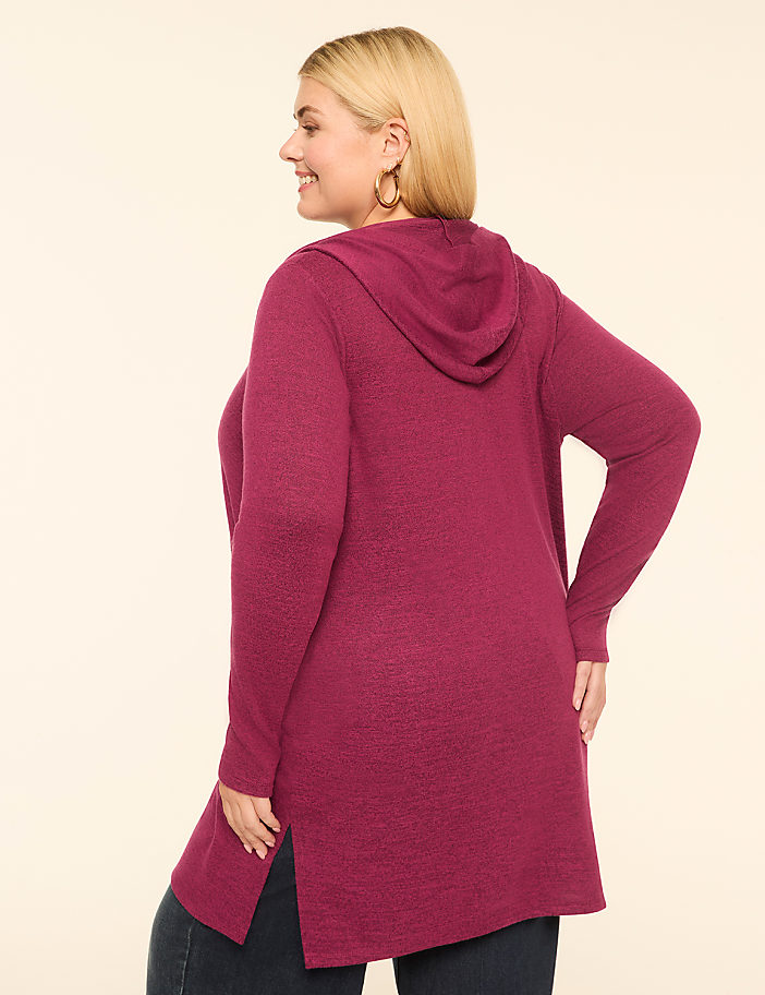 A woman in a magenta hooded cardigan stands against a plain, light-colored background.