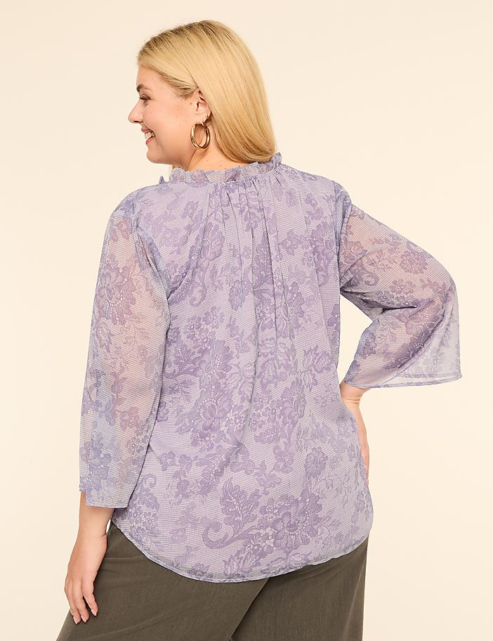 A woman in a floral print blouse stands against a plain, light-colored background.