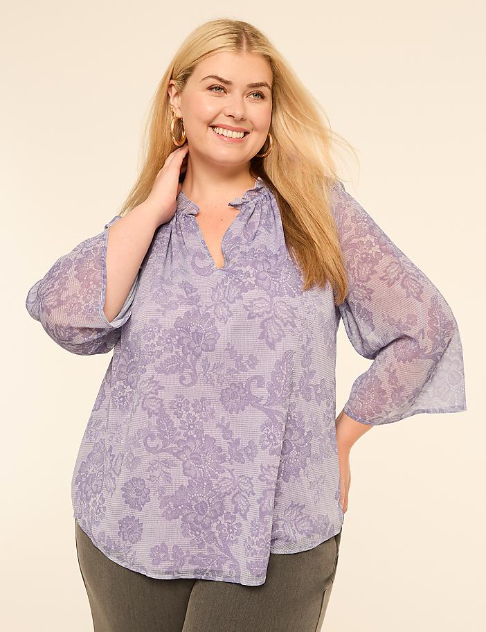 A smiling woman in a floral blouse poses against a plain, light-colored background.
