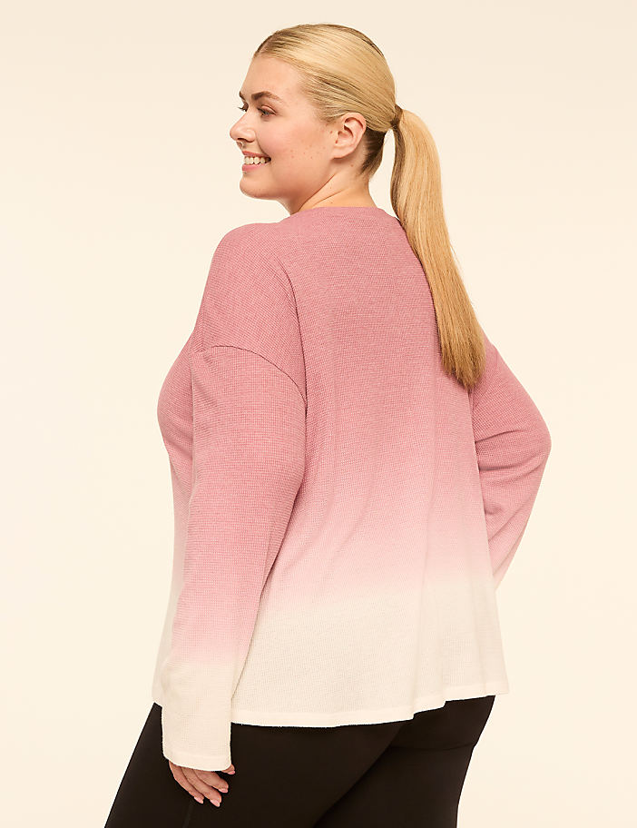 A woman in a pink and white ombre sweater and black leggings stands against a plain, light-colored background.
