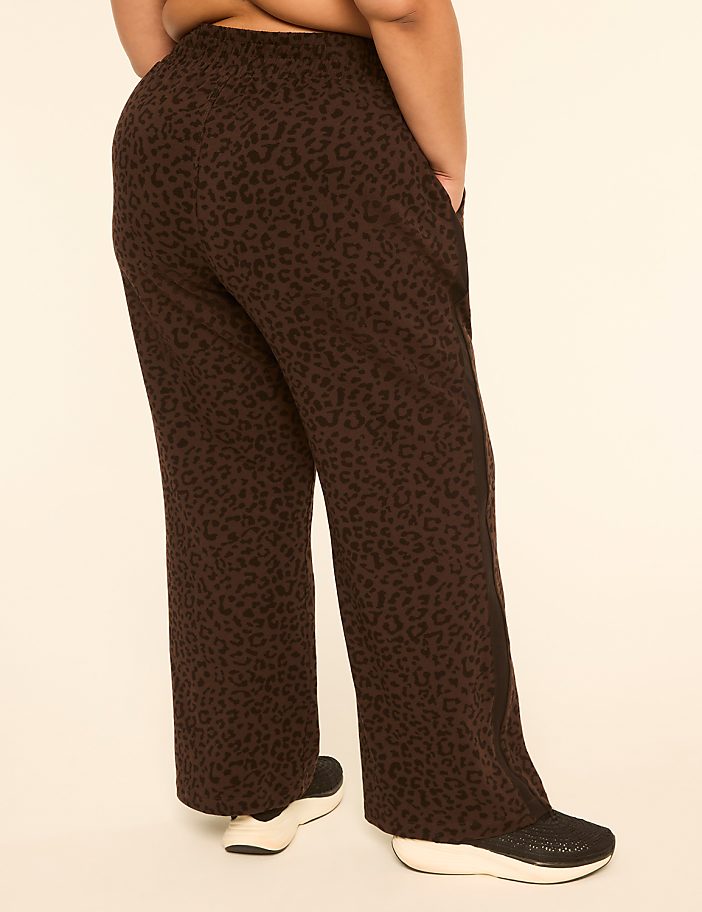 A person wearing brown leopard-print pants stands against a plain, light-colored background.