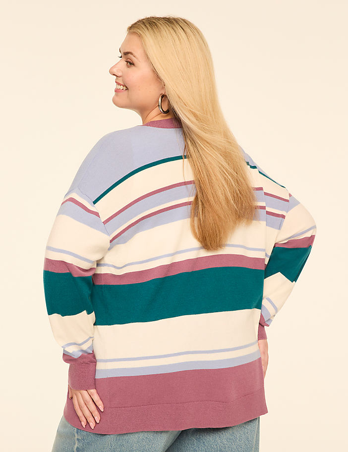 A woman in a striped sweater stands against a plain, light-colored background.
