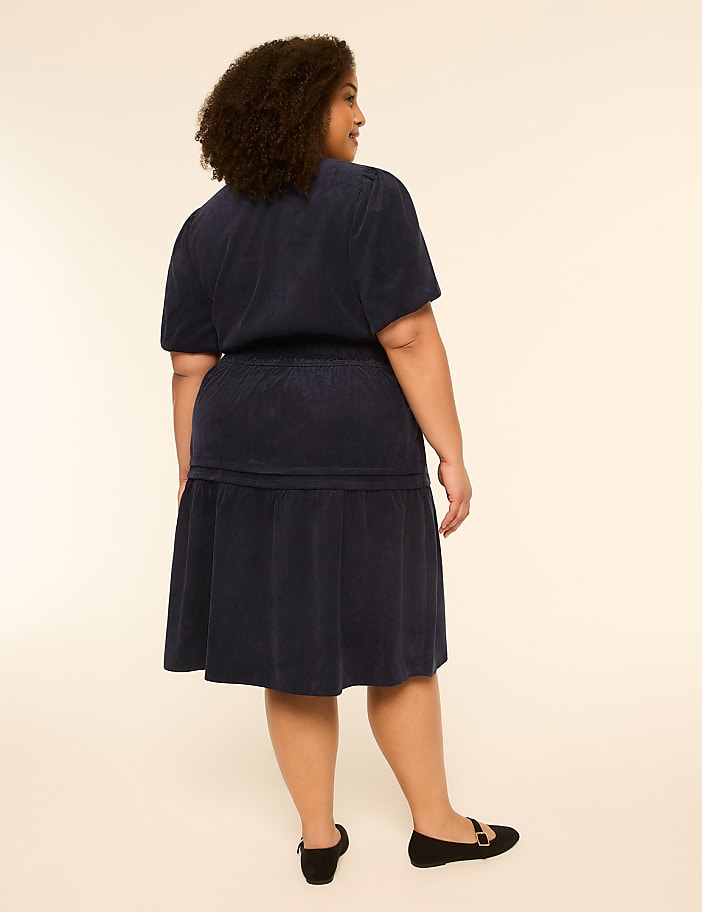 A woman in a navy blue dress stands against a plain, light-colored background.