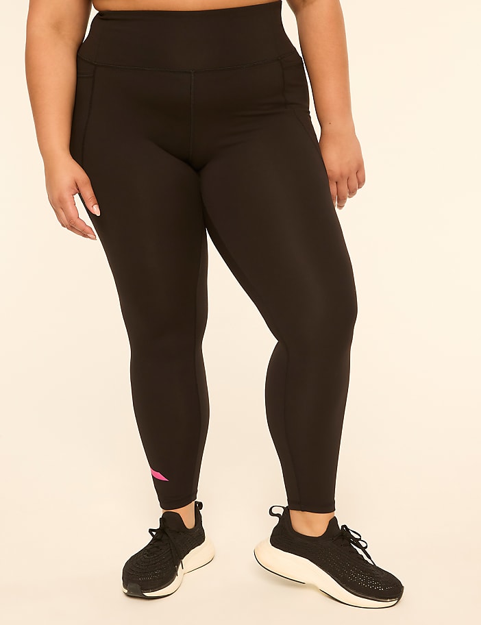 A person wearing black leggings and sneakers stands against a plain, light-colored background.