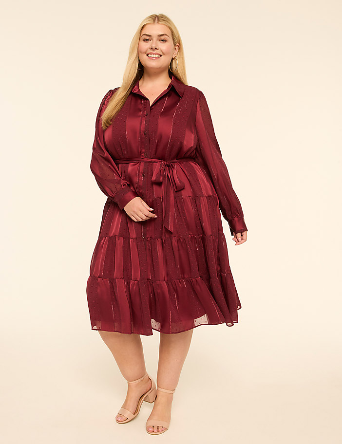 A smiling woman in a burgundy tiered dress stands against a plain cream background.