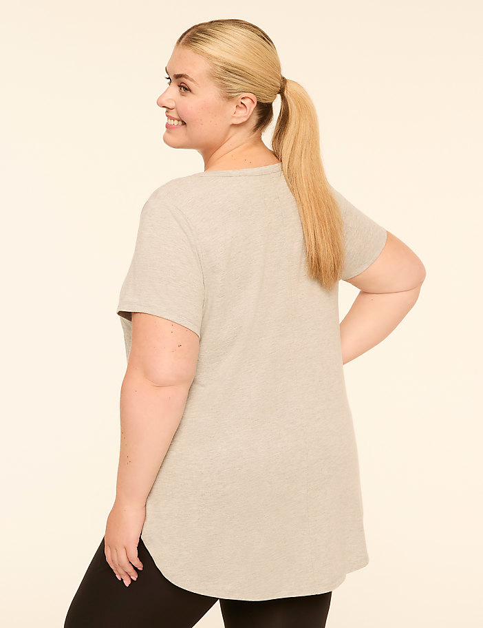 A blonde woman in a grey t-shirt and black leggings smiles as she poses against a plain, light-colored background.