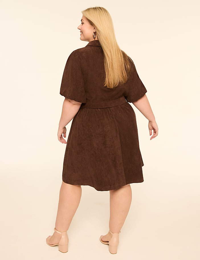 A woman in a brown dress stands against a plain, light-colored background.