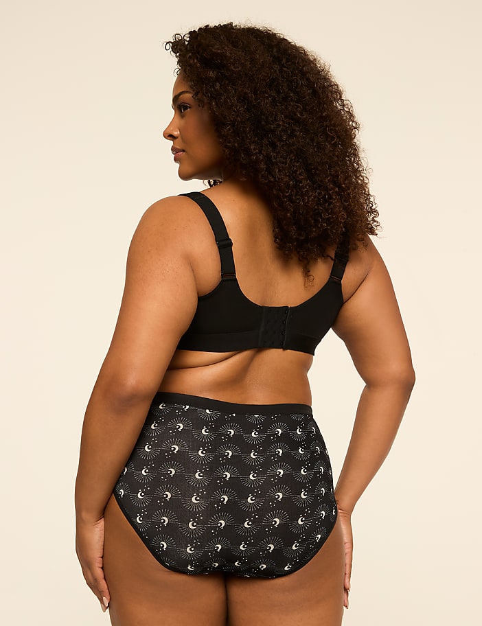 A woman in a black bra and patterned underwear stands against a plain, light-colored background.