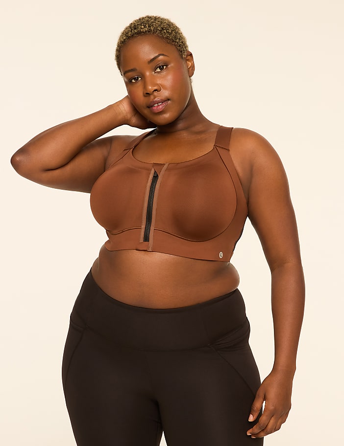 A woman with short, blonde hair poses in a brown sports bra and black leggings against a plain, light-colored background.