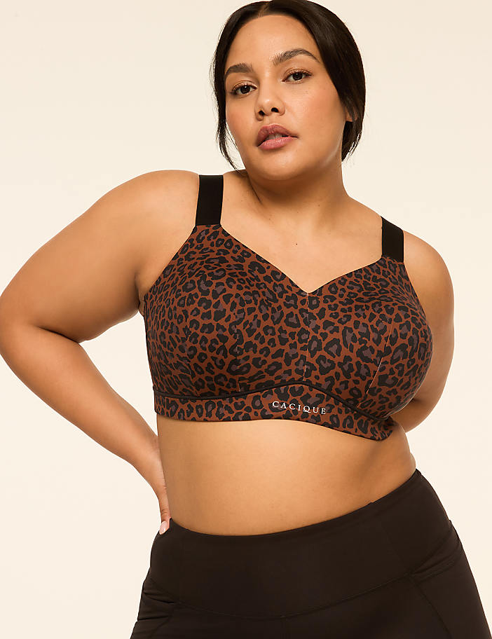 A plus-size woman with dark hair and brown eyes poses in a leopard-print sports bra and black leggings against a plain, light-colored background.