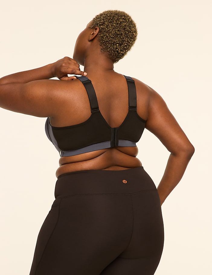 A woman in a black sports bra and leggings stands against a plain, light-colored background.