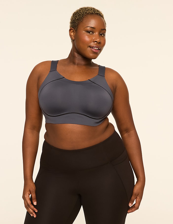 A woman with short, blonde hair and dark skin poses in a grey sports bra and black leggings against a plain, light-colored background.