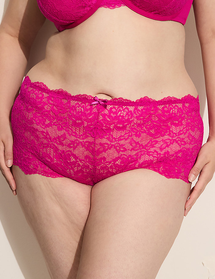 A person in bright pink lace underwear and bra stands against a plain, light-colored background.