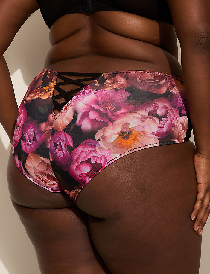 A person's lower back and buttocks are shown in the foreground, wearing floral-patterned underwear with a criss-cross detail, against a plain, light-colored background.
