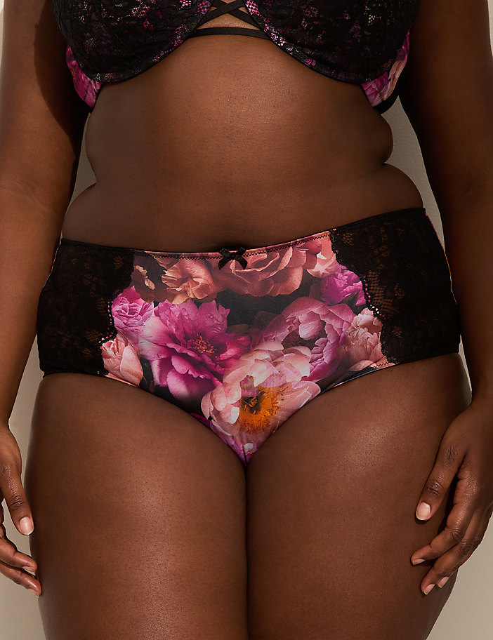 A person in floral-patterned underwear and a black lace bra stands against a plain background.