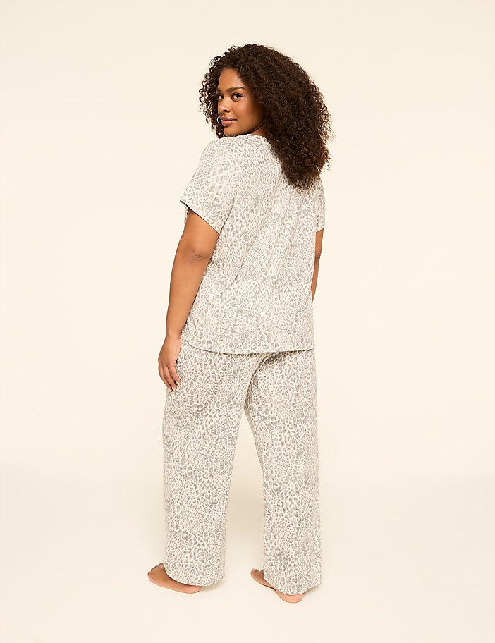 A woman in leopard-print pajamas stands against a plain, light-colored background.