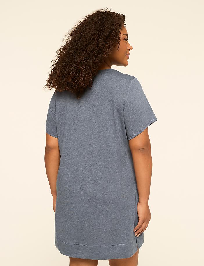 A woman in a blue t-shirt dress stands against a plain, light-colored background.