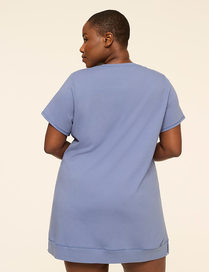 A woman in a blue t-shirt dress stands against a plain, light-colored background.