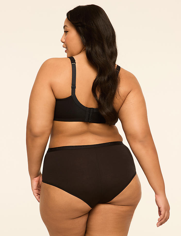 A woman in black lingerie stands against a plain, light-colored background.