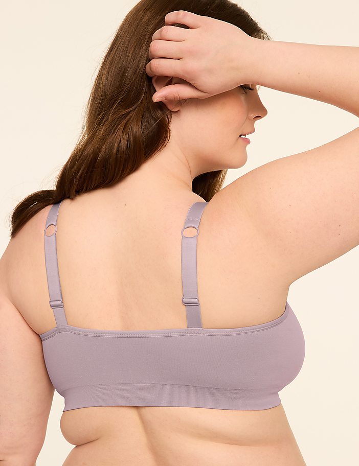 A woman in a light purple bra is shown from the back, with her arm raised to her head, against a plain, light-colored background.