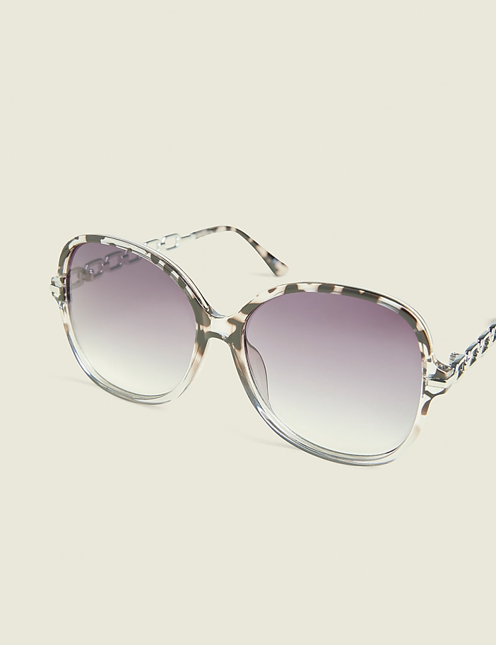 Oversized, leopard-print sunglasses with gradient lenses rest against a plain, light-colored background.