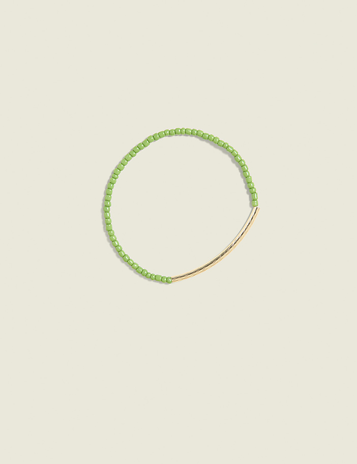 A delicate green beaded bracelet with a gold bar accent rests on a pale green background.