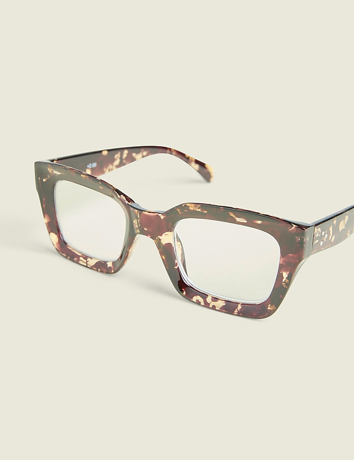 Tortoiseshell glasses with clear lenses rest on a plain, light-colored surface.