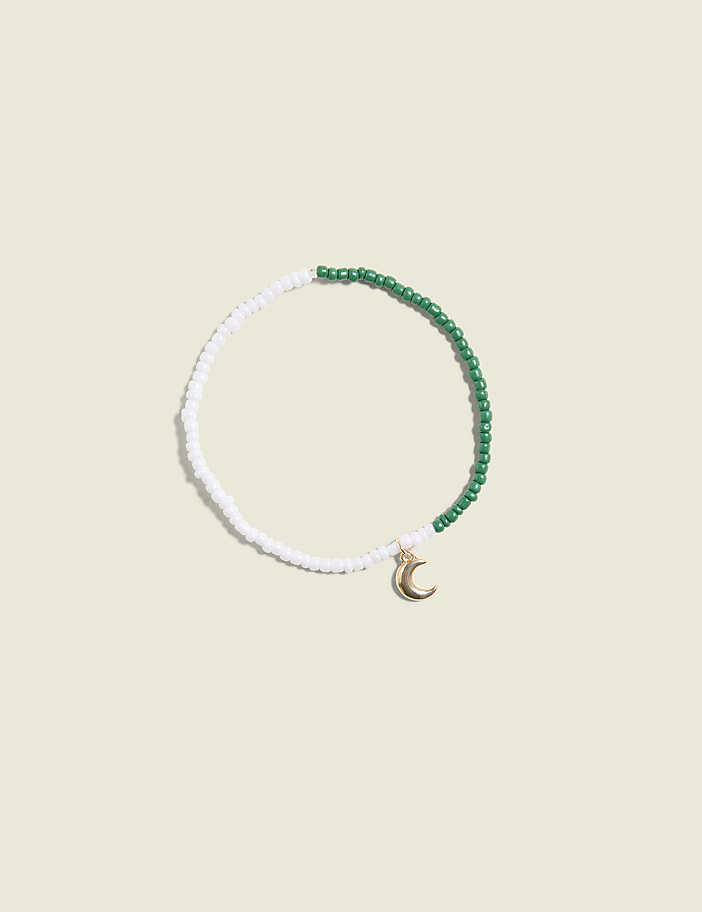 A beaded bracelet with a crescent moon charm rests on a plain, light-colored background.