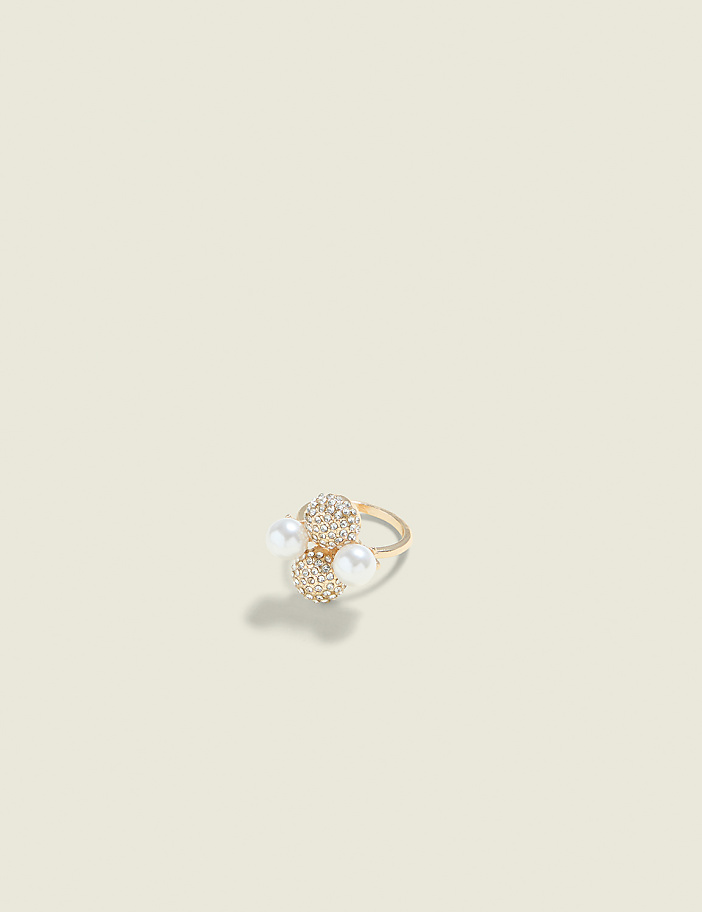 A gold ring with pearl and diamond accents rests on a plain, light-colored background.