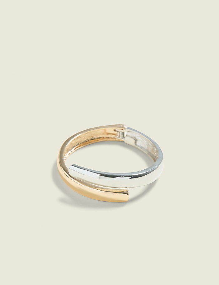 A gold and silver crossover bangle rests on a pale beige background.