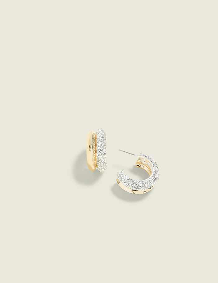 A pair of gold hoop earrings encrusted with small diamonds rests on a pale yellow background.
