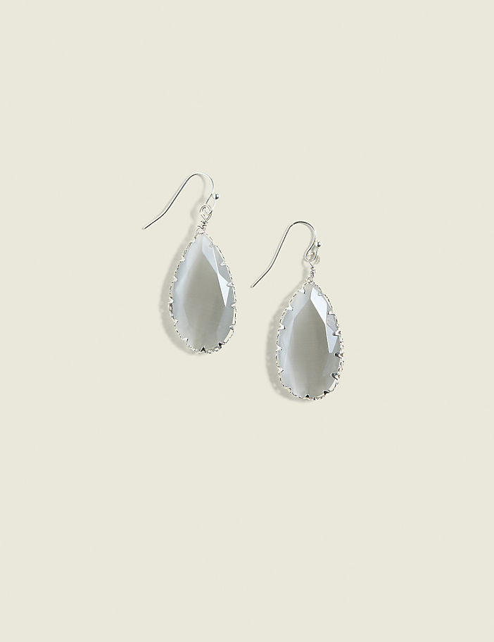 A pair of teardrop-shaped gray gemstone earrings with silver settings hang against a plain, light beige background.