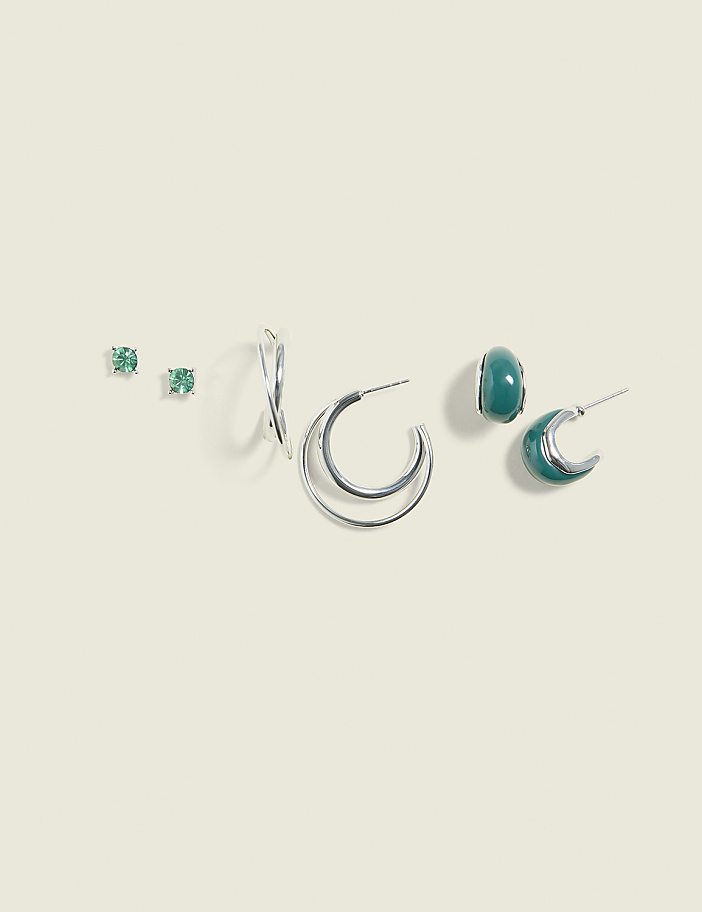 A collection of silver and green earrings are arranged on a pale green background.