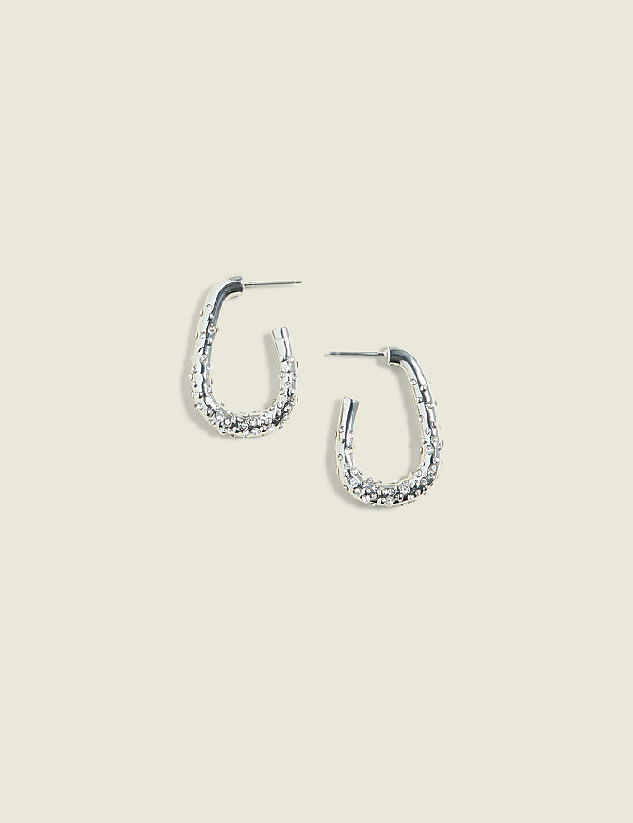 A pair of textured silver hoop earrings rests on a pale, textured background.