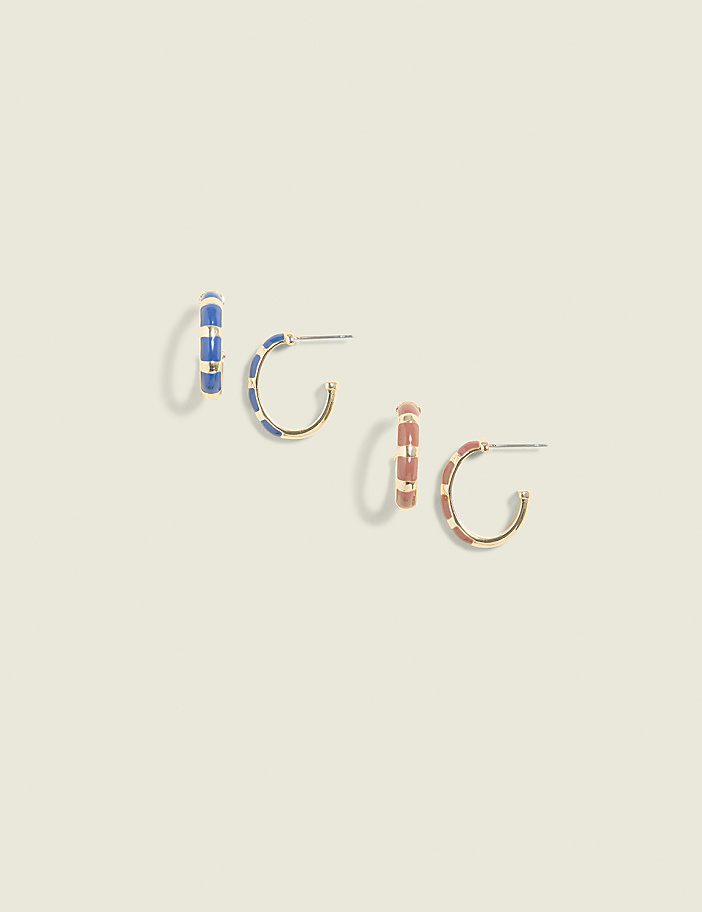 Two pairs of gold hoop earrings, one blue and white striped and the other pink and white striped, are arranged on a plain, light beige background.