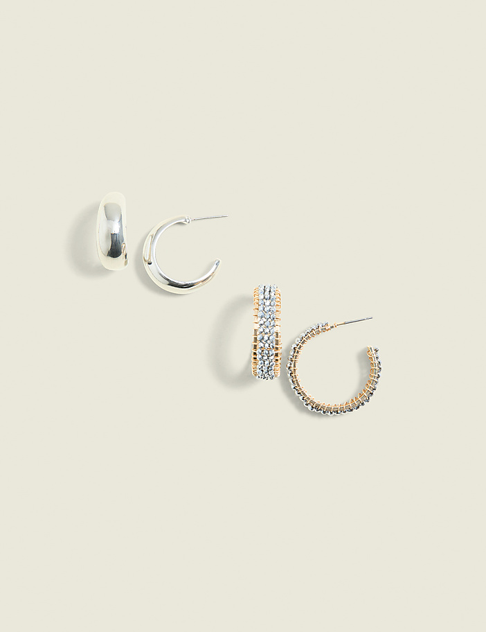 Four pairs of assorted hoop earrings, two silver and two gold-toned with embellishments, are arranged on a pale yellow background.