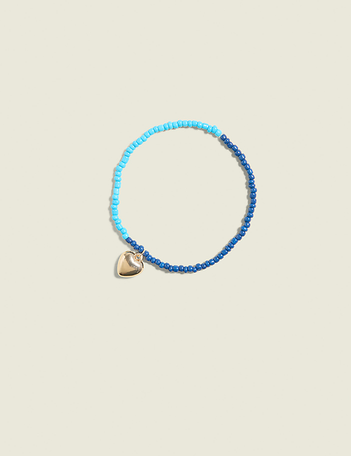 A beaded bracelet with a heart charm rests on a pale yellow background.