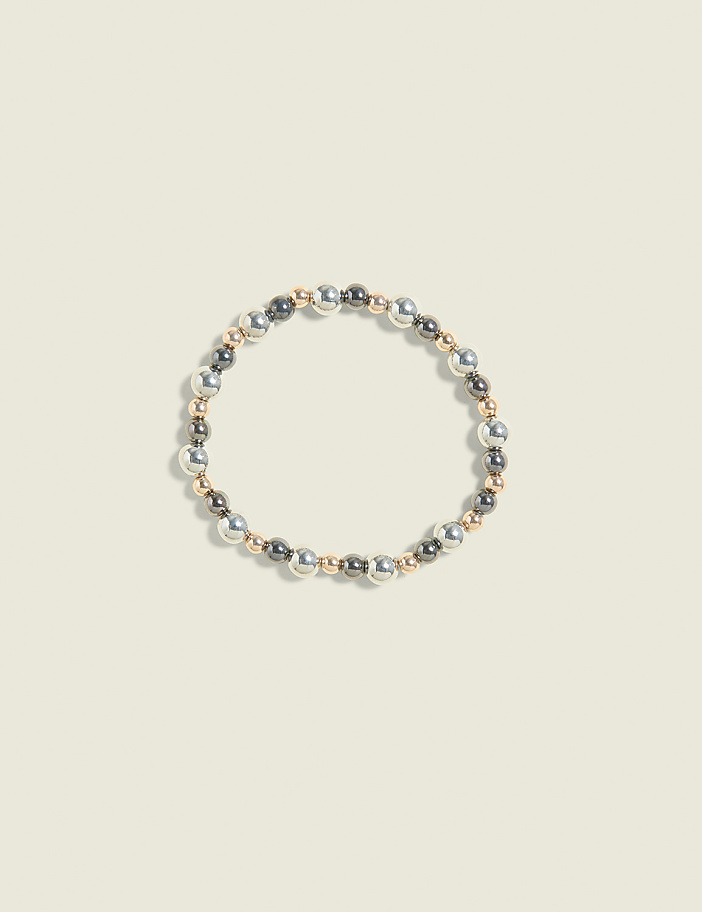 A bracelet of silver, gold, and gray beads is centered on a pale yellow background.