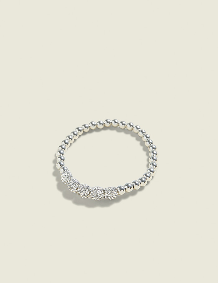 A silver beaded ring with four sparkling gemstones sits on a pale, textured background.