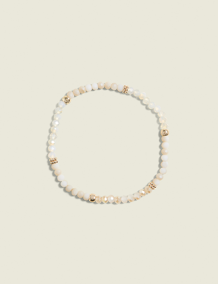 A delicate bracelet with cream-colored beads and gold accents rests on a pale, textured background.
