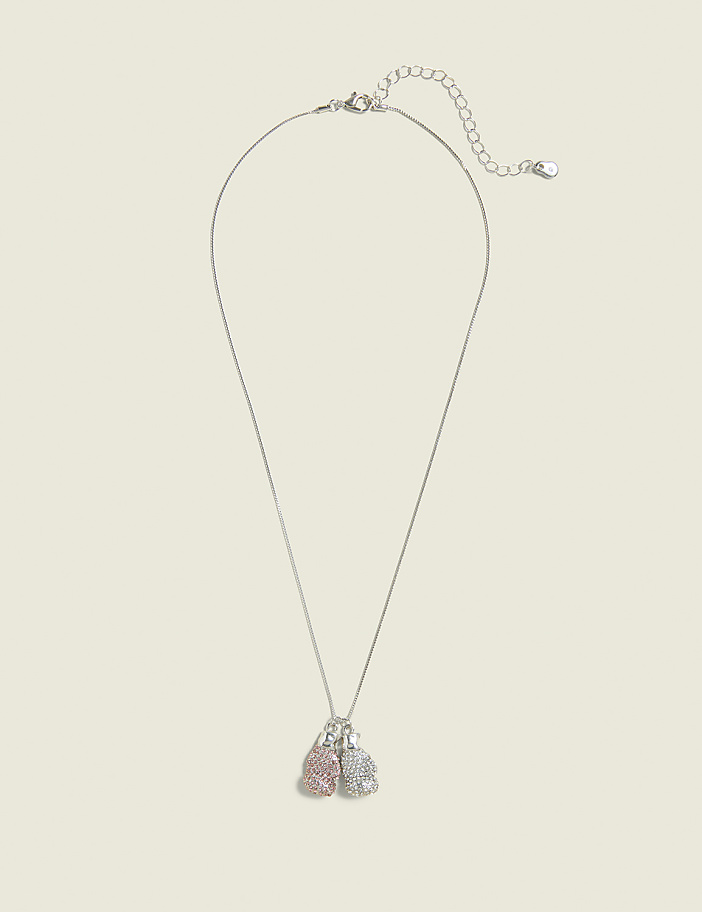 A delicate silver necklace with two small, sparkling boxing glove charms, one pink and one silver, hangs against a plain, light beige background.