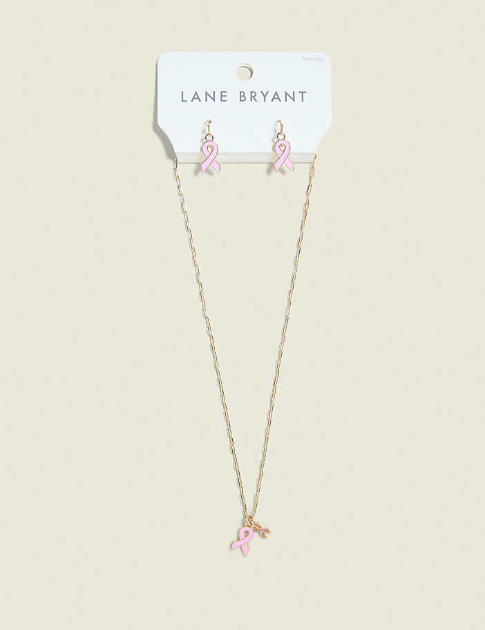 A gold necklace with a pink ribbon charm and matching pink ribbon earrings hang from a Lane Bryant card against a plain, light brown background.
