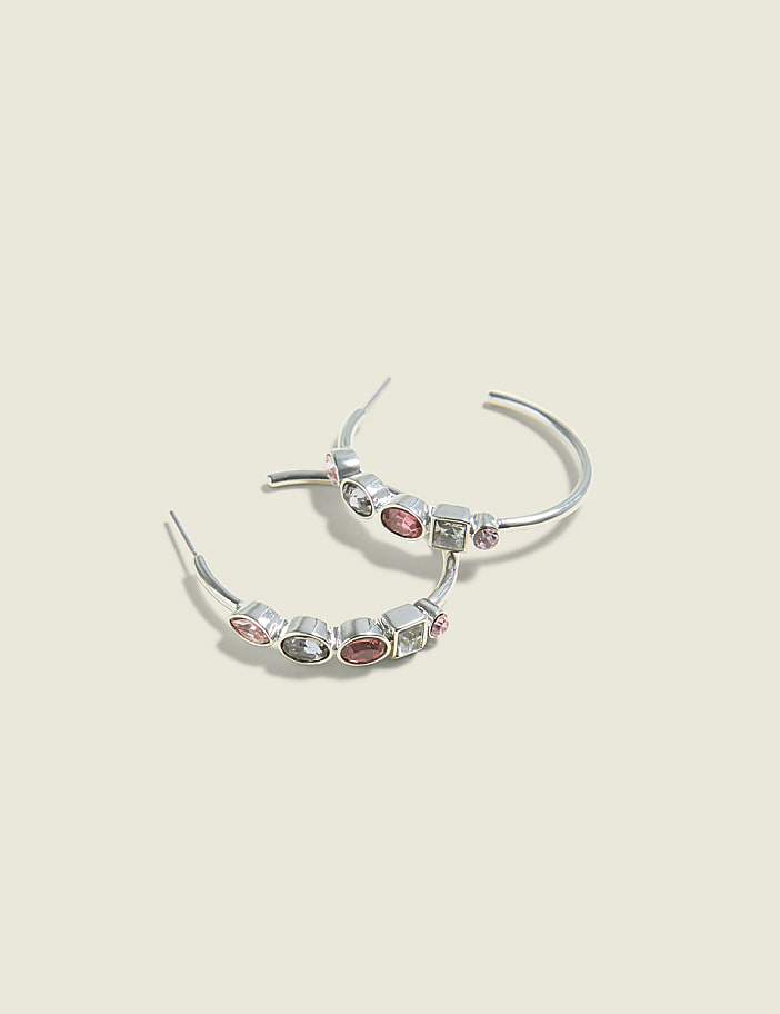 A pair of silver hoop earrings with colorful gemstones are displayed against a soft, light beige background.