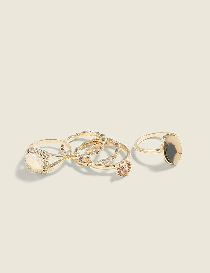 A collection of gold rings, some with stones and intricate designs, are arranged on a plain, light-colored background.