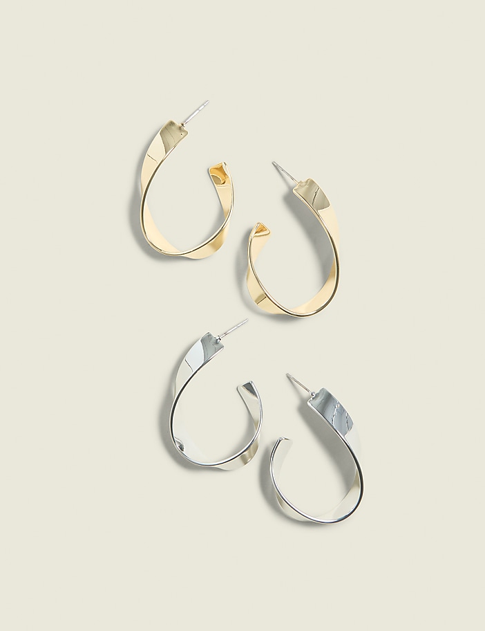 Two pairs of twisted hoop earrings, one gold and one silver, rest on a pale, neutral background.